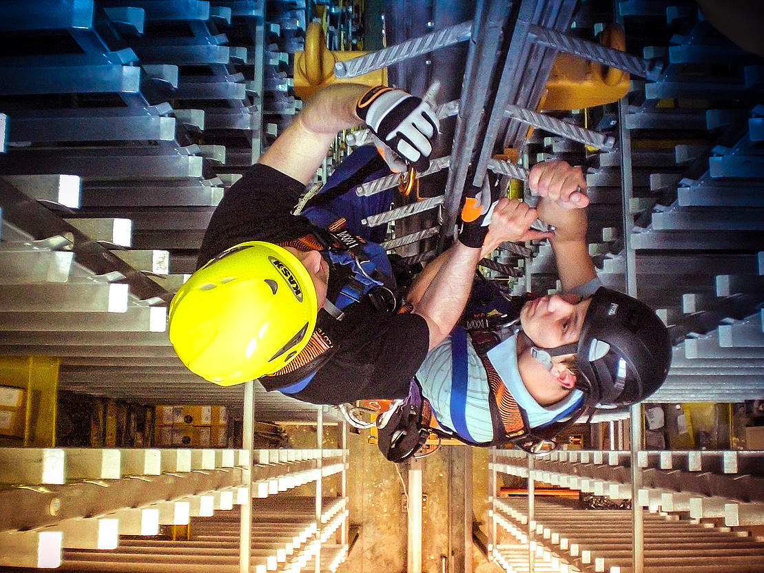 Rettung aus Steigleitersystemen – Praxisübung Zwei Teilnehmende mit Helm und Sicherungsgurt üben die Personenrettung an einer Steigleiter.